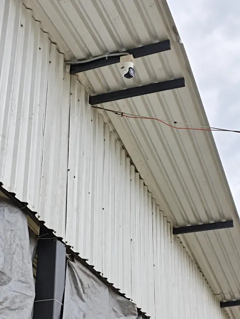 Cámara de seguridad fijada a un soporte bajo una cubierta de lámina junto a la fachada.