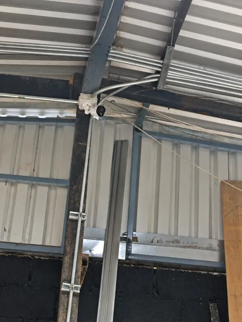 Cámara instalada junto a una viga y canalización metálica bajo un techo de lámina.