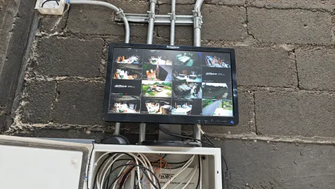 Monitor de videovigilancia con múltiples canales sobre un gabinete de conexiones abierto.